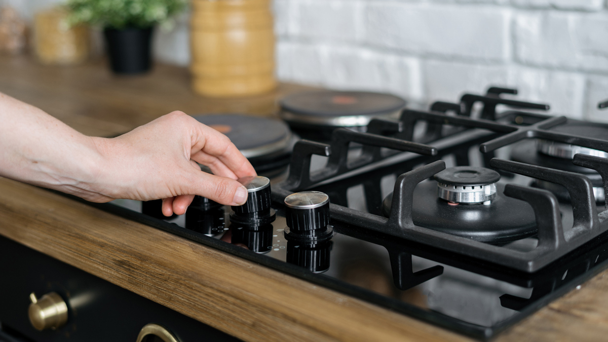 person adjusting the knobs on a gas cooktop