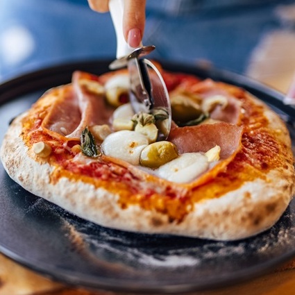 close-up of a pizza slicer cutting a wood-fired pizza