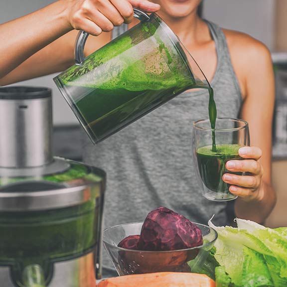 woman using juicer to make green juice sq