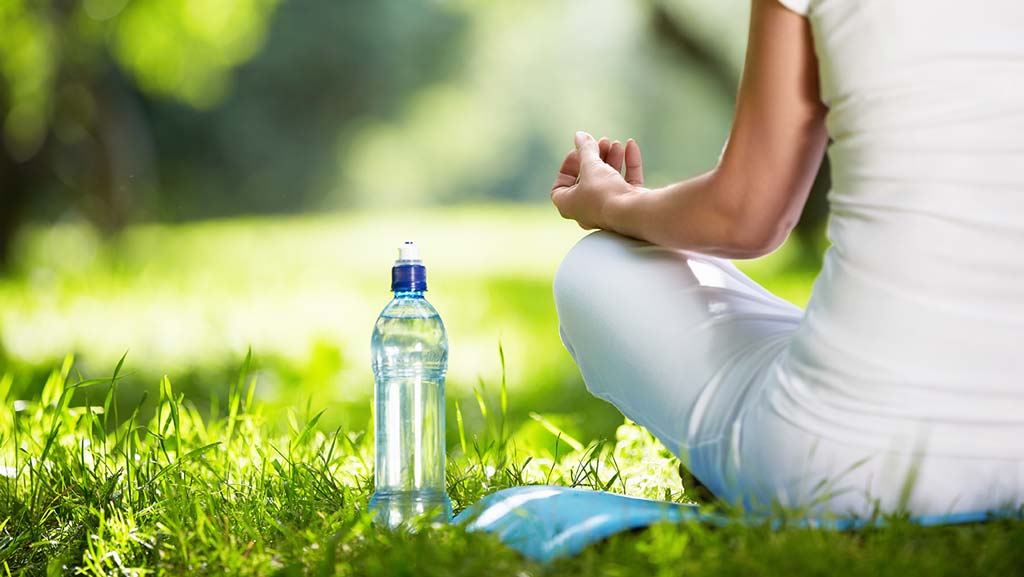 woman sitting meditating with bottle of water