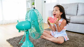 young girl sitting in front of electric fan