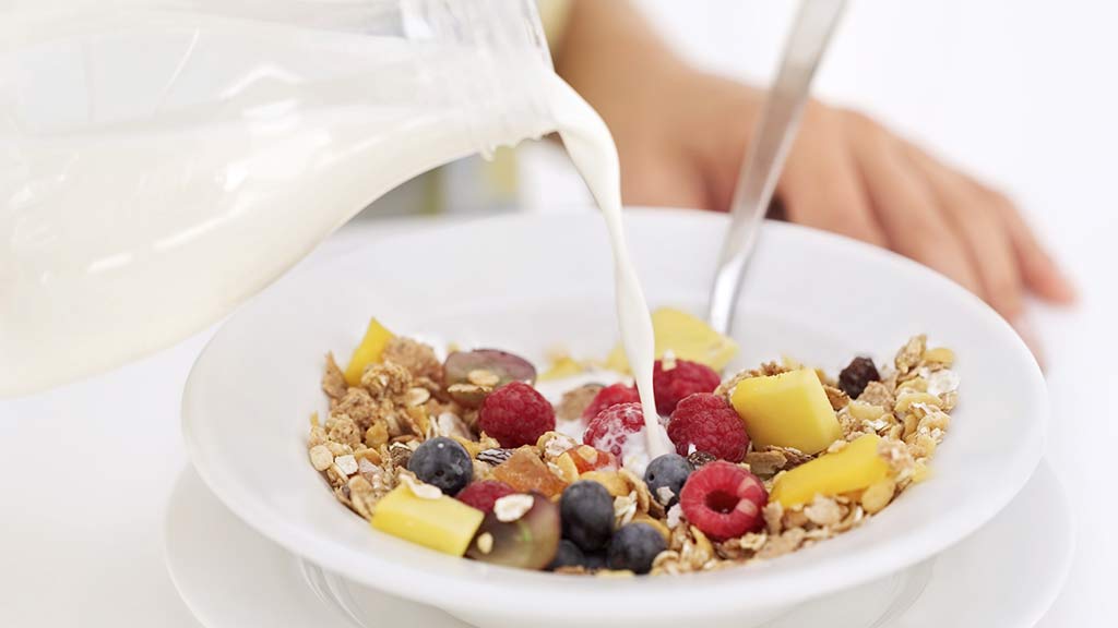 milk being poured onto fruit and museli