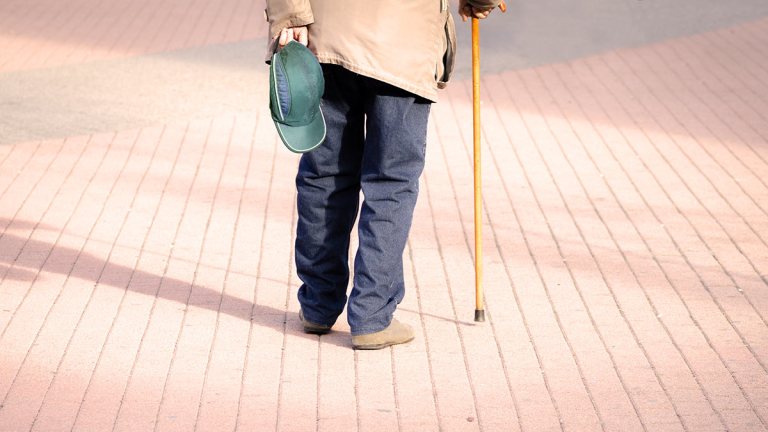 senior man with cane walking through paved park
