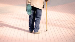 senior man with cane walking through paved park