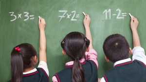 Three young students doing maths problems on a blackboard