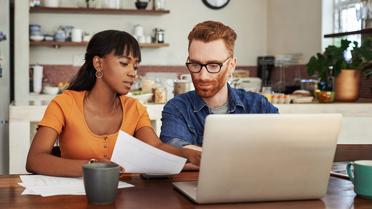 couple paying bills on laptop in kitchen