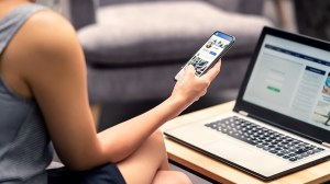 person_with_laptop_checking_social_media_on_smartphone