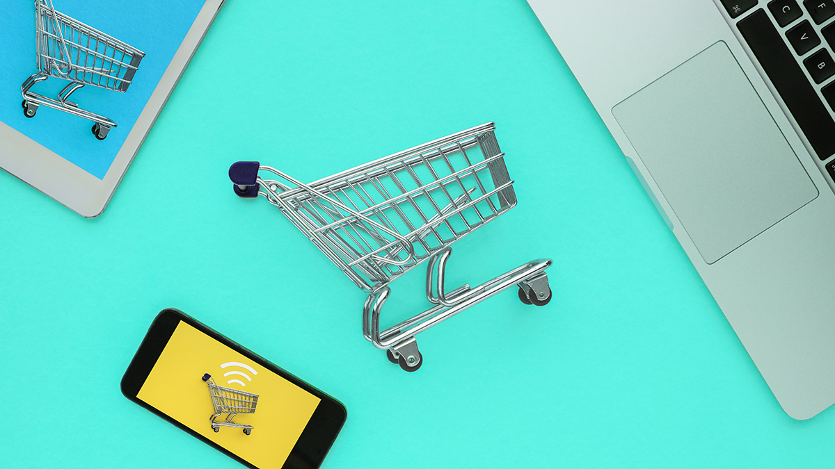 a laptop, tablet and smartphone with miniature shopping trolleys next to them