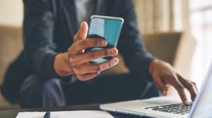 person_looking_at_smartphone_while_typing_code_on_their_laptop