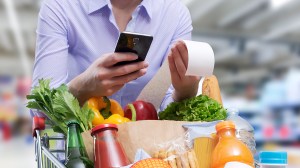 person_in_supermarket_with_full_trolley_checking_receipt_with_smartphone