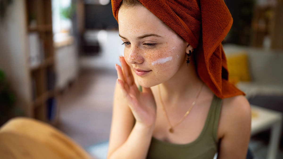 teenager applying facial cream in front of mirror