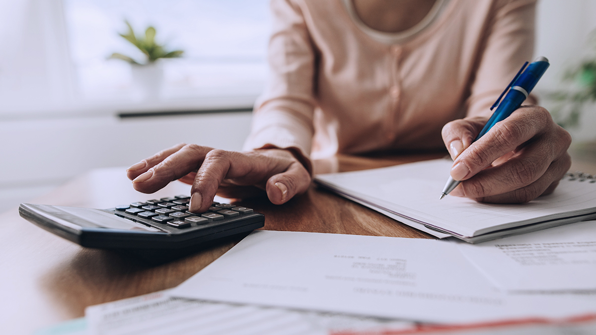 person sitting at a desk calculating costs with a pen, paper and calculator