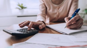 person sitting at a desk calculating costs with a pen, paper and calculator