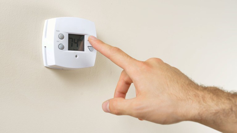 hand adjusting digital thermostat on wall