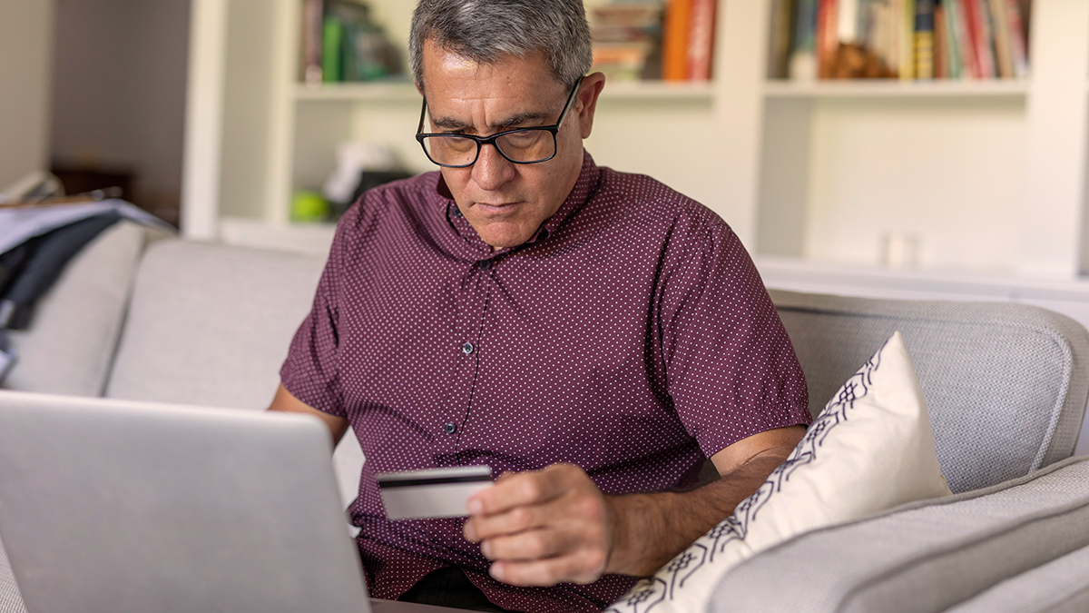 person sitting on a lounge in front of a laptop holding a credit card