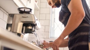 person cleaning milk frother spout on coffee machine