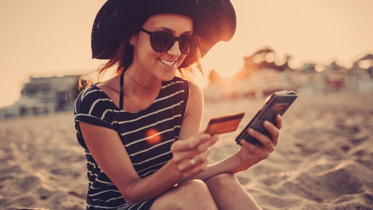 person on beach holiday using credit card on phone