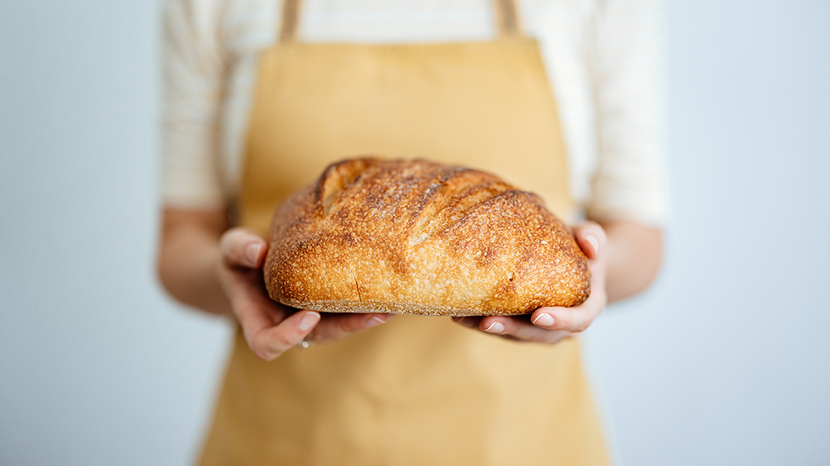 person wearing an apron holding a loaf of sourdough bread