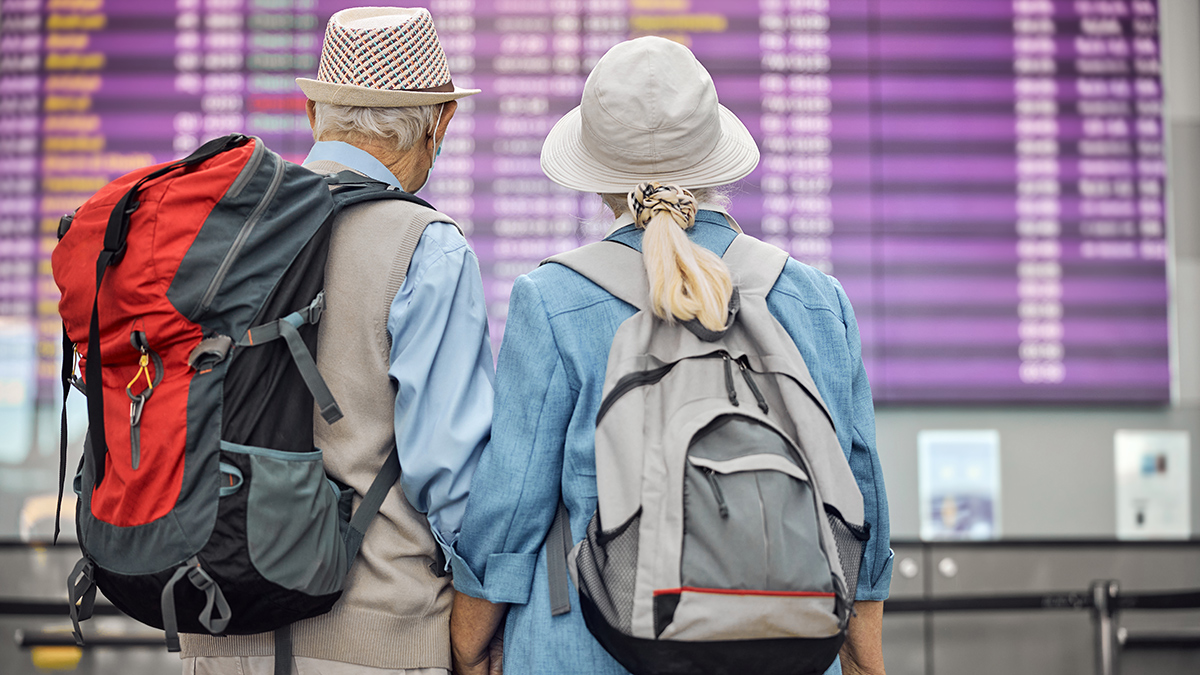 senior_couple_looking_at_departure_flights_board_in_airport