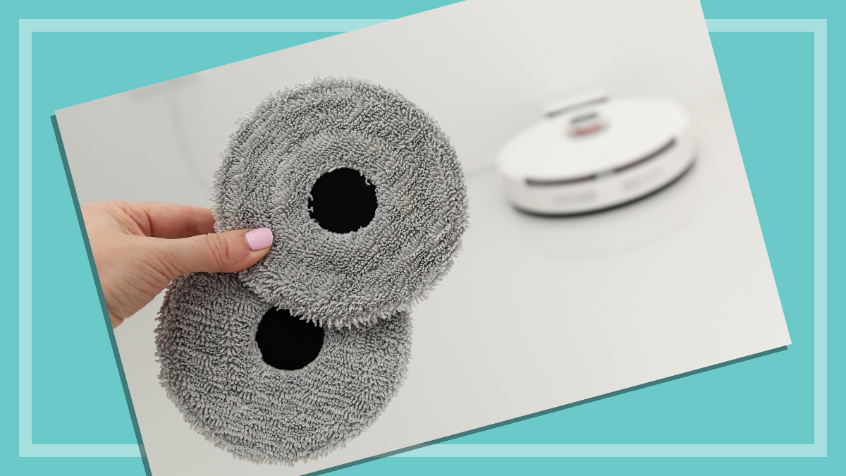 hand holding mopping pads with robot vacuum in background