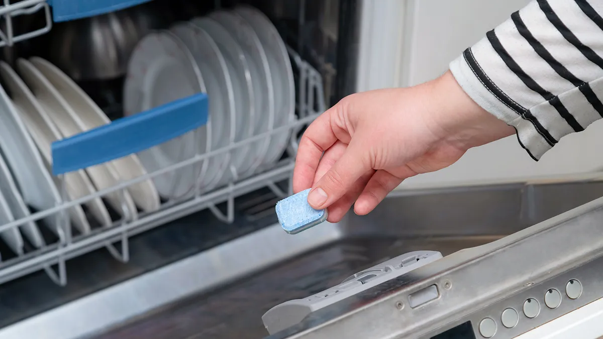 person throwing detergent tablet onto the floor of the dishwasher