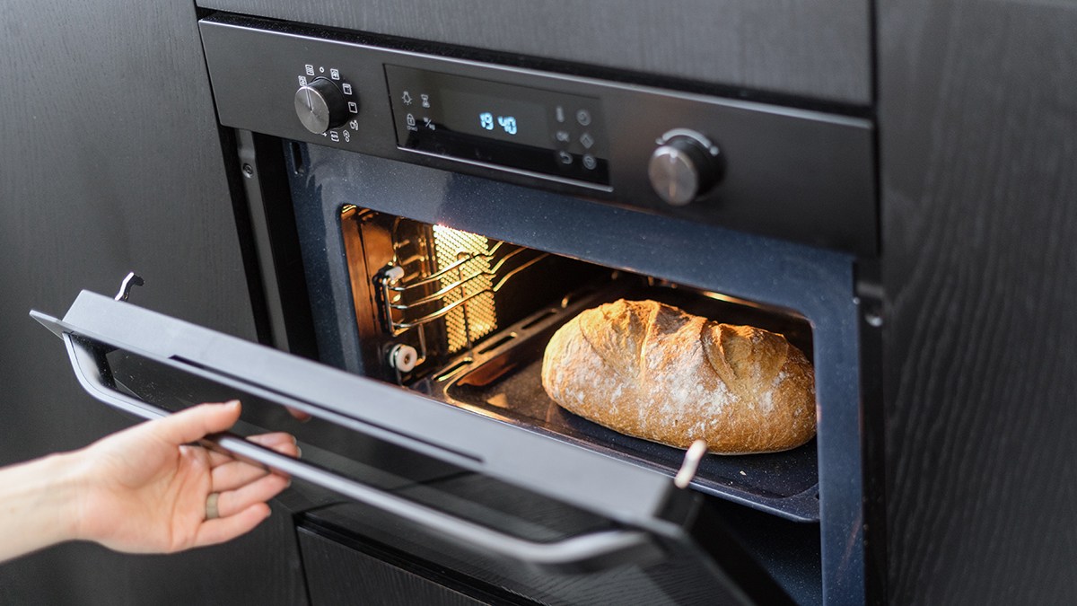 Person opening an oven door to reveal sourdough bread.